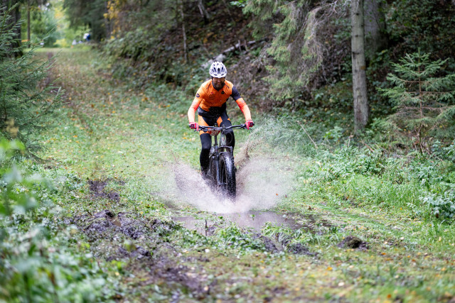 single e-bike racer moving though the puddle on a forest trail